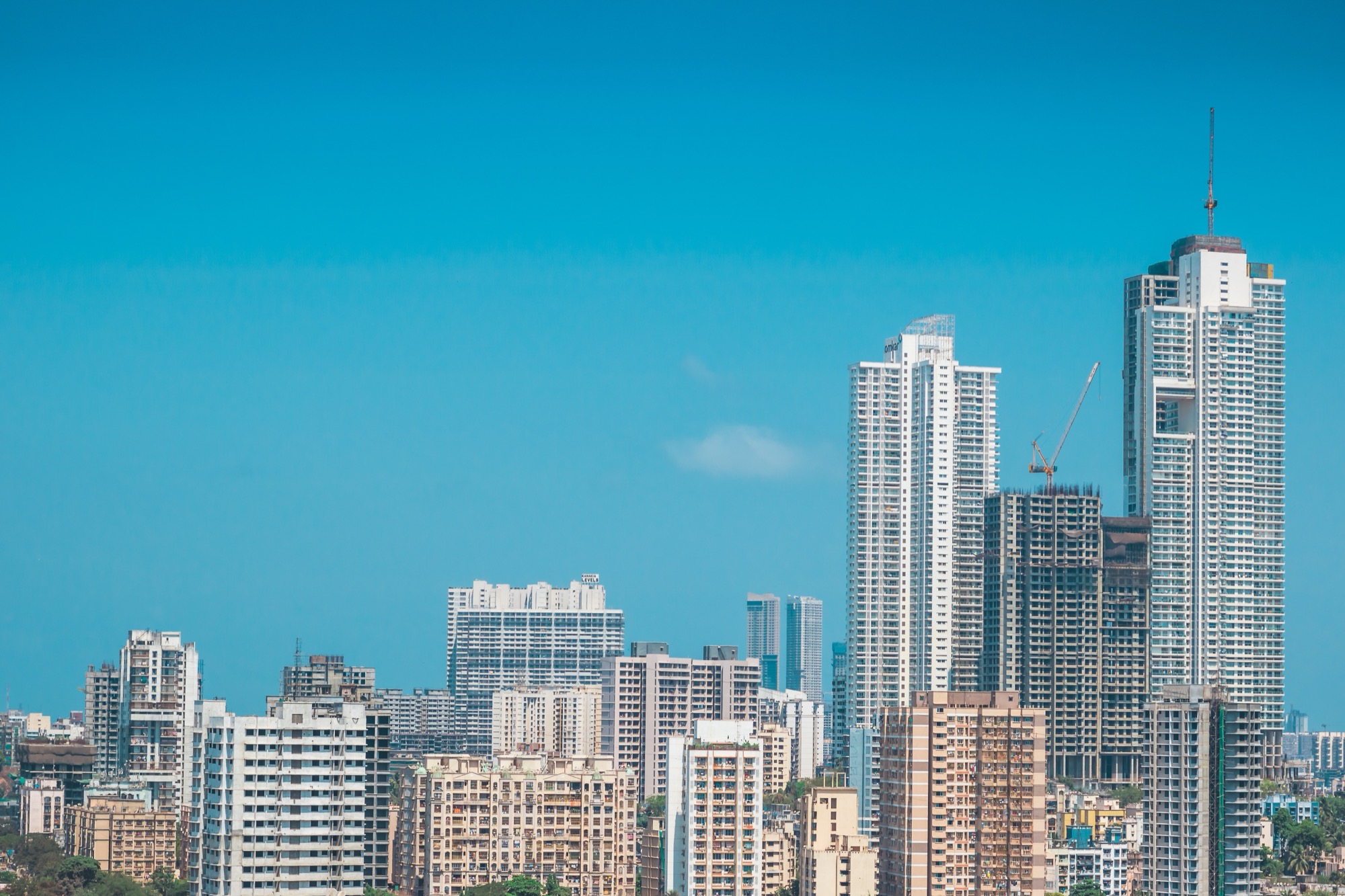 A dense Indian city skyline of high-rise buildings under a blue sky