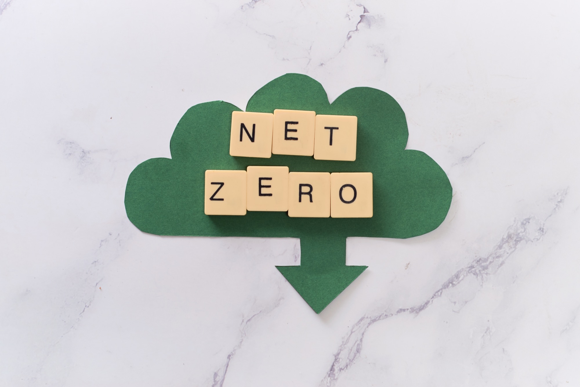 Paper tiles spelling "NET ZERO" arranged on a green paper cloud cutout