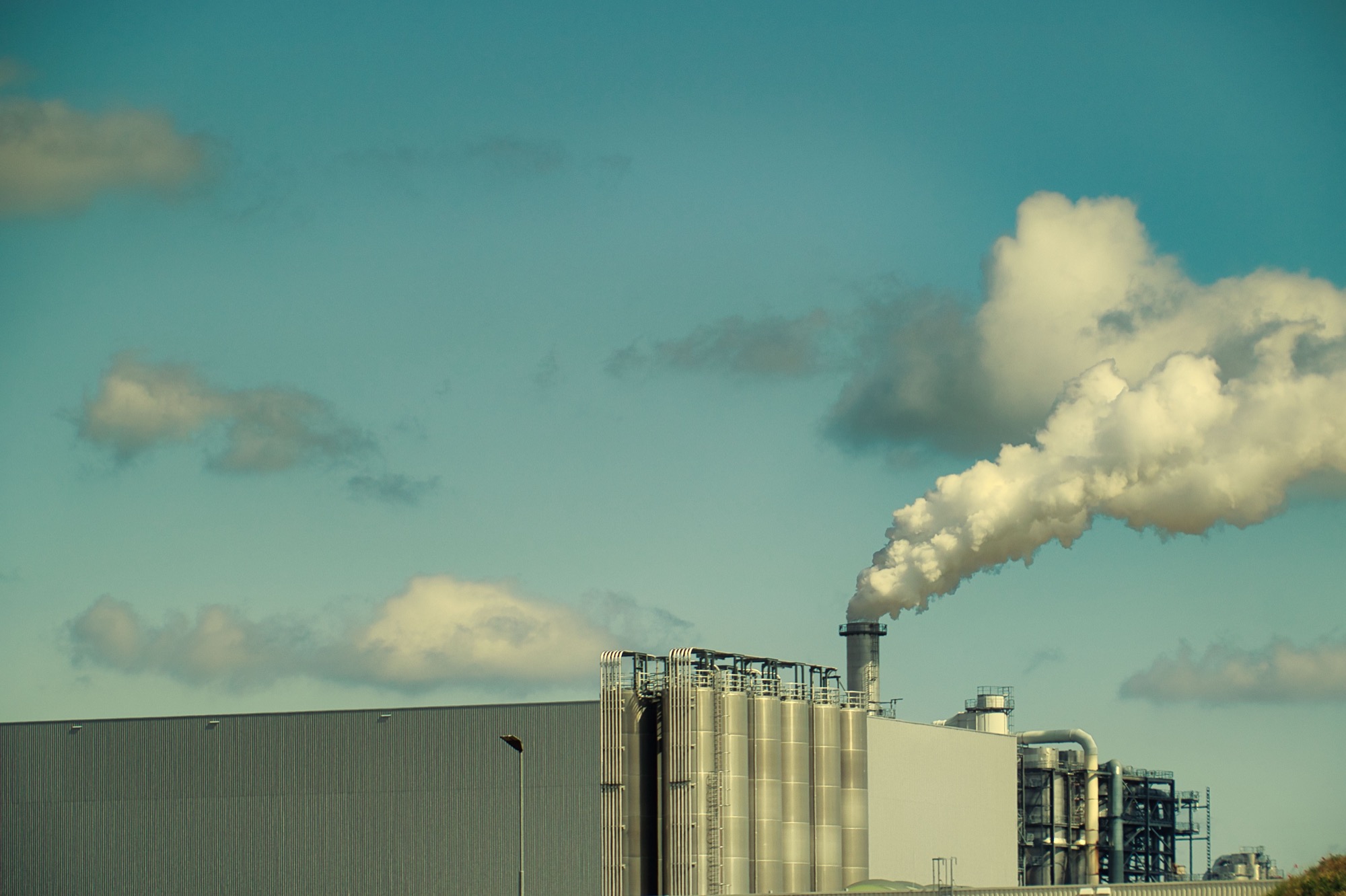 Smoke rising from a factory chimney against a blue sky, representing industrial GHG emissions
