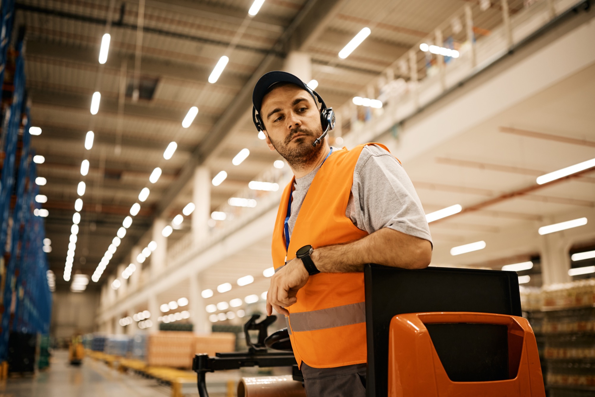 A warehouse worker in a safety vest operating a pallet jack in a storage facility
