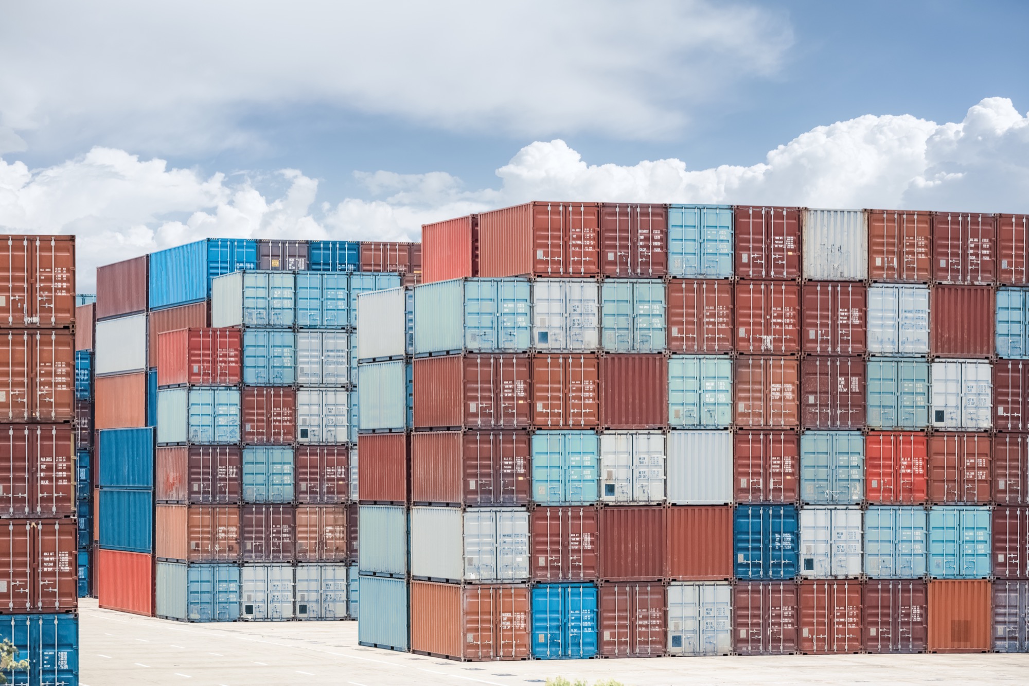 Colorful stacked shipping containers at a port under a cloudy sky